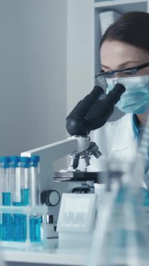 Laboratuvar önlüğü giymiş kendini adamış bir bilim adamı güçlü bir mikroskop altında ileri düzey bir laboratuvardaki araştırmaların önemini vurgulayarak gelecekteki yenilik ve keşifleri örnek alarak test örnekleri üzerinde çalışıyor.