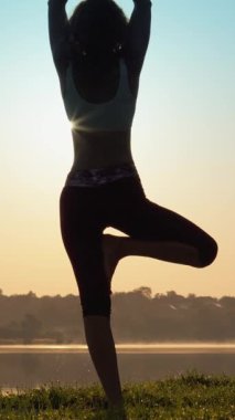Gün doğumunda yoga yapan huzurlu bir kadın silueti, mükemmel bir şekilde somutlaştırıcı sükunet ve denge, güzel manzaralı göl kenarı zeminine karşı, refah ve uyumu teşvik eder.