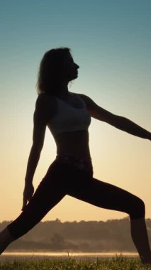 Bir kadın, dinginliği, farkındalığı ve doğanın güzelliğiyle olan derin bağlantısını sembolize eden canlı ve nefes kesici bir gündoğumu sırasında nazikçe yoga yapar.