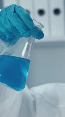 Bir laboratuvar ortamında, koruyucu ekipman içinde kendini adamış bir bilim adamı canlı mavi bir çözeltiye sahip cam şişeyi inceliyor, hassasiyeti ve güvenli deneyler için hayati önem taşıyor.