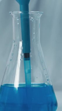 Yetenekli bir laboratuar teknisyeni, kalibre edilmiş bir pipetten, önemli bilimsel araştırmaları yürütürken hassas olduğunu gösteren bir test tüpüne canlı mavi bir sıvı aktarıyor.
