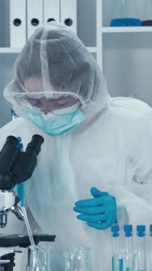 Steril bir laboratuvarda, koruyucu ekipman içinde kendini adamış bir bilim adamı test tüplerini inceler ve mikroskop kullanır. Gelişmiş araştırma tekniklerini göstererek bilimsel keşifleri engeller.