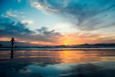 Deniz kenarında gün batımı. Su aynasında gökyüzünün yansımaları. Suda bir banyonun silueti. Santos şehri, Brezilya.