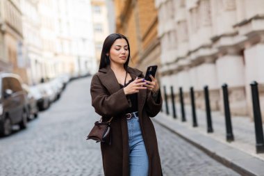 Prag 'ın bulanık caddesinde cep telefonu kullanan esmer, modaya uygun bir kadın.