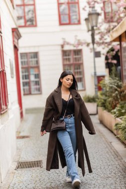 Güz giysileri içinde genç ve güzel bir kadın Prag 'da dar bir sokakta yürüyor.