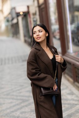Güz ceketli güzel esmer kadın çapraz vücut tutuyor ve Prag 'ın bulanık caddesine bakıyor.
