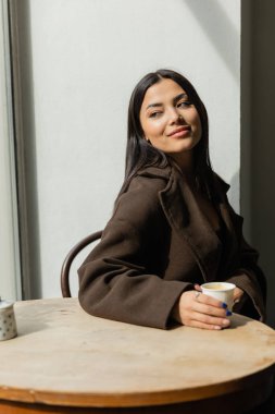 Prag Kafe 'de elinde kağıt bardakla oturan modaya uygun giyinmiş esmer kadın.