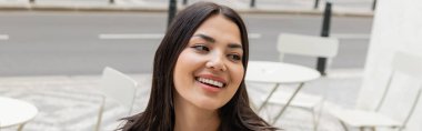 Portrait of young brunette woman smiling on urban street, banner  clipart