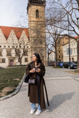 Prag 'da şehir caddesinde elinde kahve tutan modaya uyan genç bir kadın. 