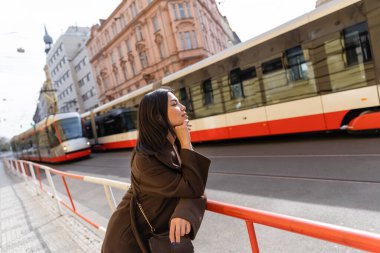 Prag caddesinde tramvaylara bakan ceketli esmer kadın. 