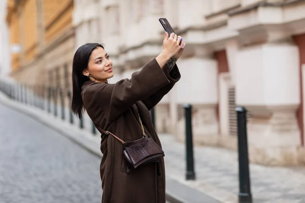 stock image smiling brunette woman in trendy coat taking selfie on mobile phone in prague