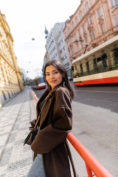 Smiling woman in coat looking at camera on urban street in Prague 
