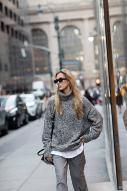 Kış süveteri ve güneş gözlüğü takan güzel bir kadın New York 'ta şehir sokağında el ele ayakta duruyor. 