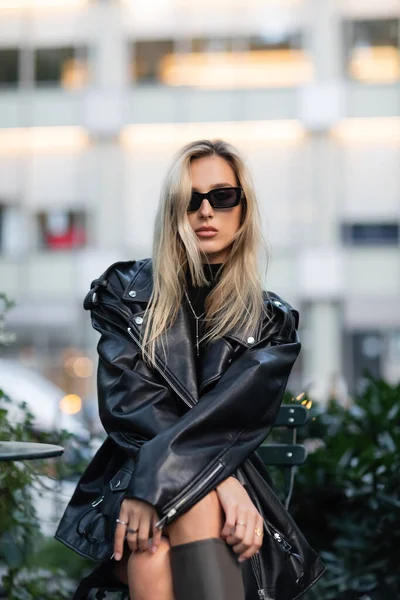 stock image young blonde woman in black leather jacket and sunglasses sitting in outdoor cafe 