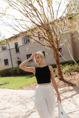 blonde woman in black tank top standing near house in Miami  clipart