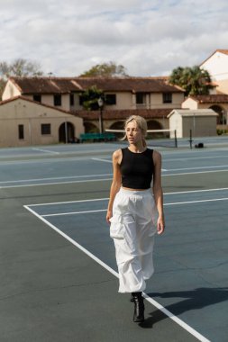 Miami 'de tenis kortunun yakınında beyaz kargo pantolonlu genç bir kadın yürüyor. 