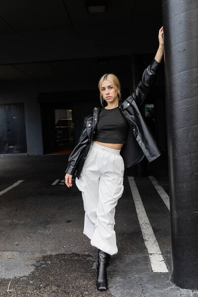 full length of young blonde woman in leather shirt jacket and cargo pants standing on street in Miami 