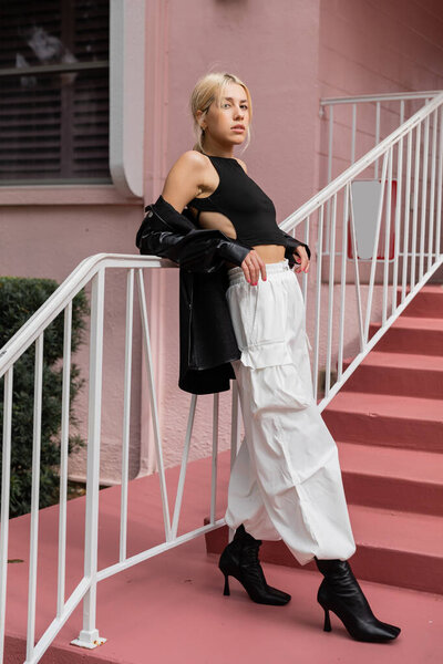 full length of blonde woman in black tank top and cargo pants standing on pink stairs in Miami 