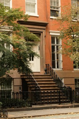 Beyaz pencereli tuğla ev ve New York 'ta sonbahar ağaçlarının yanındaki merdivenli giriş.