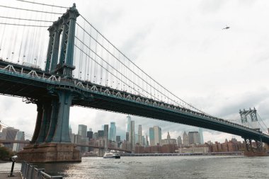 New York 'ta bulutlu gökyüzü altında Manhattan Köprüsü ve modern gökdelenlerin manzarası