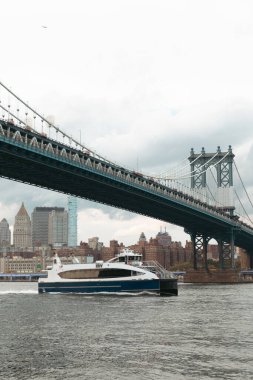 modern boat under Manhattan bridge near skyscrapers of New York City on background clipart