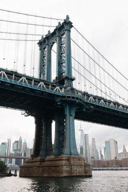 Manhattan bridge and cityscape of New York City skyscrapers under cloudy sky clipart