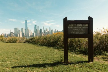 NEW YORK, USA - OCTOBER 13, 2022: board with liberty state park lettering on green lawn and cityscape with skyscrapers on background