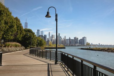 walkway on embankment of Hudson river with scenic view of skyscrapers of New York City clipart