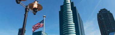 New York 'ta mavi gökdelenlerin altında fener ve ABD bayrağının alçak açılı görüntüsü.