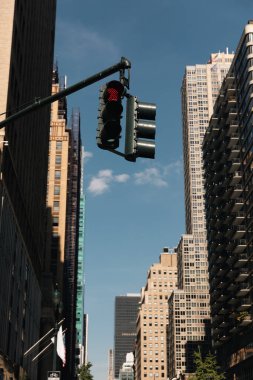 traffic light on city street near modern buildings in New York City against blue sky