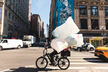 NEW YORK, ABD - 13 Ekim 2022: selofan çantalı teslimatçı şehir caddesinin kavşağında bisiklet sürüyor