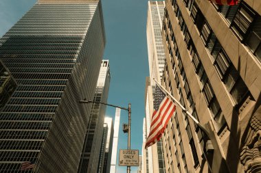 New York 'taki modern binaların yakınındaki ABD bayrağı ve yol tabelasının alçak açılı görüntüsü