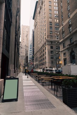 Kafe terasında boş masalar ve New York caddesinde boş bir menü tahtası.