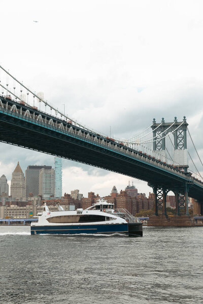 modern boat under Manhattan bridge near skyscrapers of New York City on background