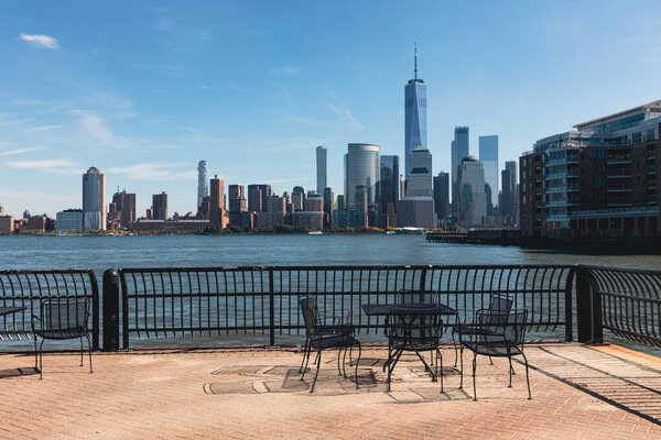 набережная со столом и стульями возле гавани и городского пейзажа Манхэттена в Нью-Йорке