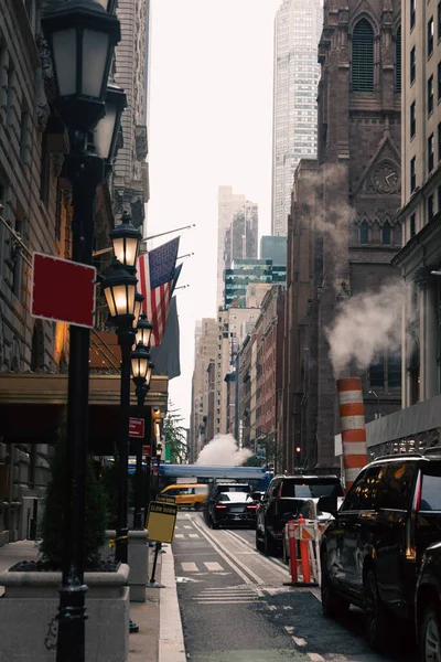 NEW YORK, USA - OCTOBER 13, 2022: narrow street with cars and lanterns near usa flags in Manhattan