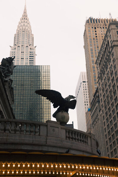 luminous garland and eagle statue on New York Grand Central Terminal near skyscrapers and Chrysler building on background