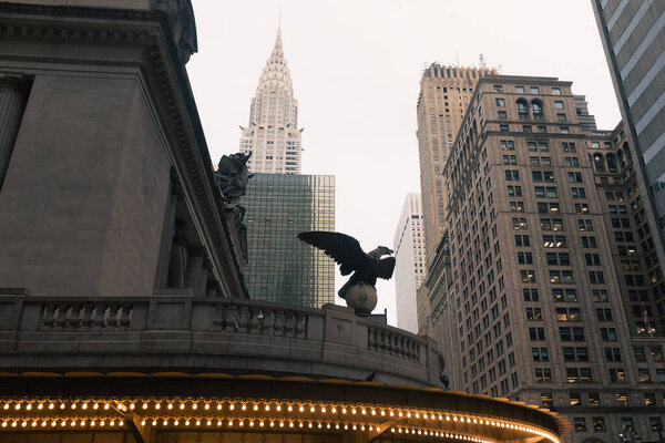 eagle statue and luminous garland on facade of Grand Central Terminal with Chrysler building on background in New York City