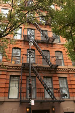 Metal balkonlu tuğla bina ve New York 'ta fener ve ağaçların yanındaki yangın merdiveni.