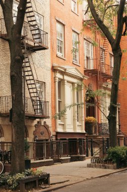 stone building with balconies and fire escape ladders near trees on sidewalk in New York City
