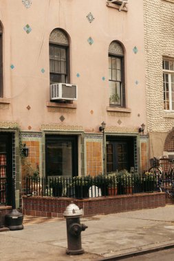 old building with arc windows near metal fence and flowerpots with plants in New York City clipart