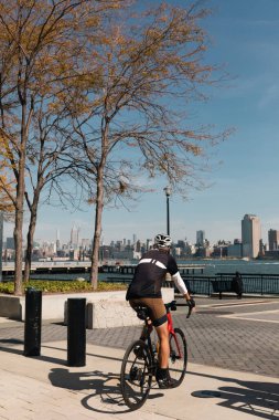NEW YORK, USA - OCTOBER 11, 2022: Man biking on Hudson river waterfront walkway at daytime  clipart