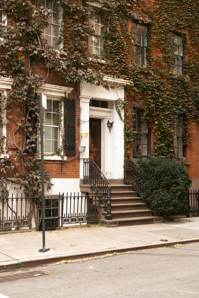 Дом с зеленым плющом и лестницей возле белого входа на улице Нью-Йорка