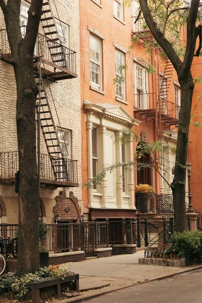 stock image stone building with balconies and fire escape ladders near trees on sidewalk in New York City