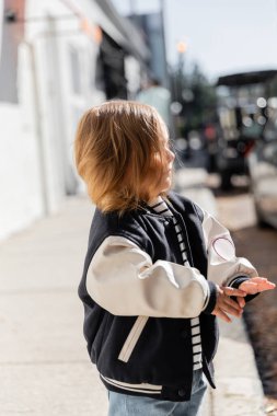 toddler girl in stylish bomber jacket walking on street in Miami  clipart