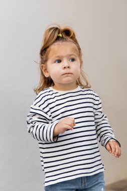 Çizgili uzun kollu gömlekli ve kot pantolonlu bebek başka tarafa bakıyor. 