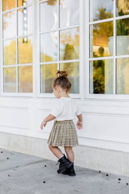 Etekli ve beyaz tişörtlü bir kız çocuğu evin yanında yürüyor. 