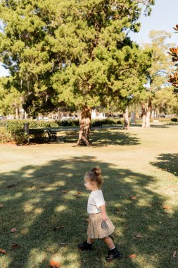 Yeşil parkta oynayan beyaz tişörtlü ve etekli neşeli kız. 