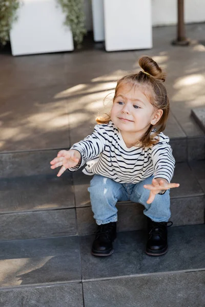 stock image baby girl in casual clothes demanding attention and gesturing while sitting on stairs near house 