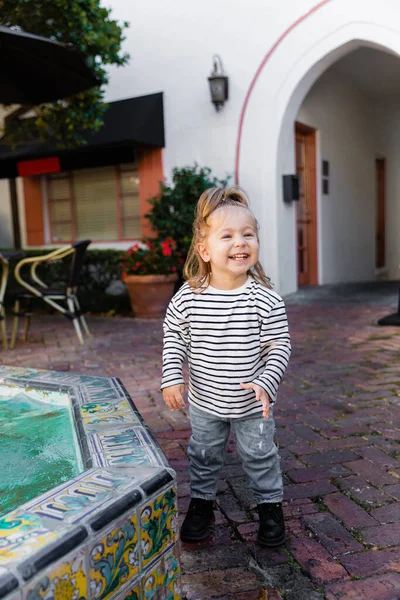 stock image happy toddler girl in striped long sleeve shirt standing near fountain in Miami 